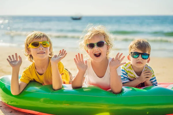 Los niños se sientan en un colchón inflable en gafas de sol contra el mar y se divierten — Foto de Stock