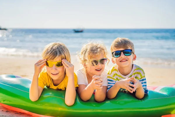 I bambini si siedono su un materasso gonfiabile in occhiali da sole contro il mare e si divertono — Foto Stock