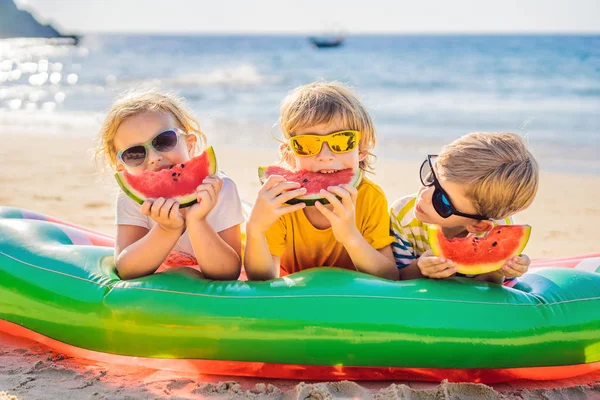 I bambini mangiano anguria sulla spiaggia in occhiali da sole — Foto Stock