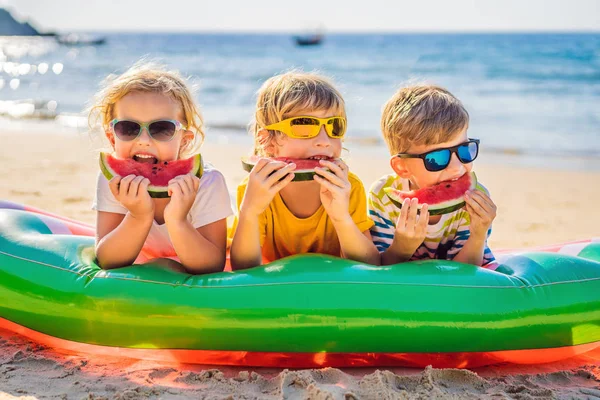 Çocuklar güneş gözlüğü ile plajda karpuz yemek