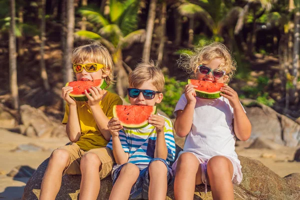 I bambini mangiano anguria sulla spiaggia in occhiali da sole — Foto Stock