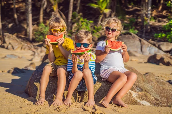 I bambini mangiano anguria sulla spiaggia in occhiali da sole — Foto Stock