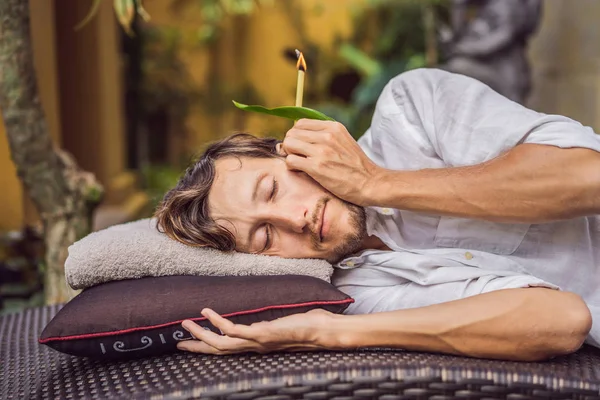 Homem tendo uma terapia de vela de ouvido contra o pano de fundo de um jardim tropical — Fotografia de Stock