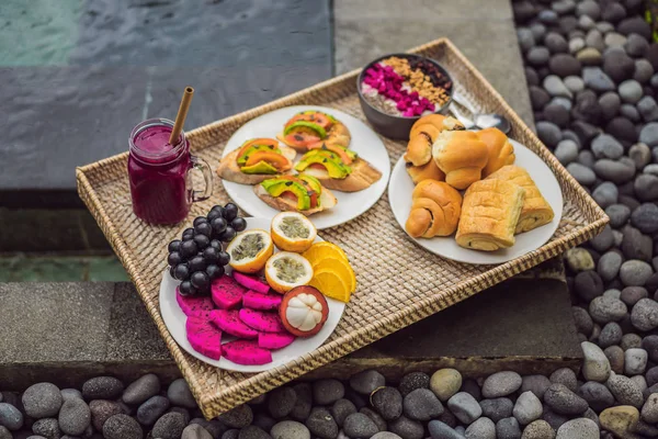 Café da manhã em uma bandeja com frutas, pães, sanduíches de abacate, tigela de smoothie na piscina. Dieta saudável de verão, café da manhã vegan. Conceito de férias saborosas — Fotografia de Stock