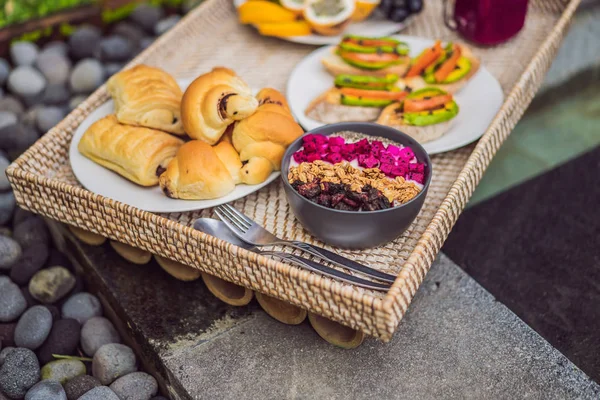 Café da manhã em uma bandeja com frutas, pães, sanduíches de abacate, tigela de smoothie na piscina. Dieta saudável de verão, café da manhã vegan. Conceito de férias saborosas — Fotografia de Stock