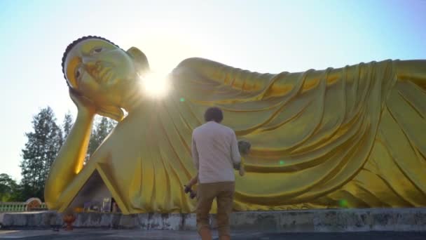 Plan au ralenti d'un jeune homme et de son petit fils s'amusant devant une statue du Bouddha couché sur l'île de Phuket. Voyager en Thaïlande concept — Video