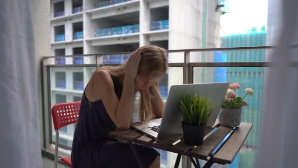 Slow Motion shot van een jonge vrouw zittend op een balkon met een notebook en die lijden aan een hard geluid geproduceerd door een bouwplaats in de buurt. Concept van geluidsoverlast in grote steden — Stockvideo