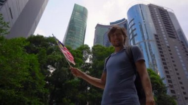 Bir akıllı telefon tutan ve arka planda gökdelenler ile Malezya bayrağı dalgalar genç bir adamın Slowmotion çekim. Malezya'ya seyahat konsepti