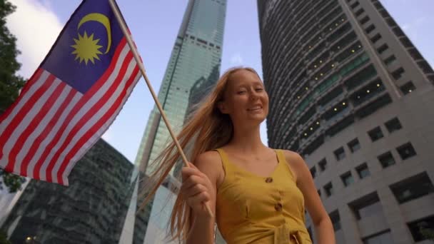 Langsom skud af en ung kvinde, der vinker malaysisk flag med skyskrabere på en baggrund. Rejse til Malaysia koncept – Stock-video