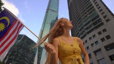 Arka planda gökdelenler ile Malezya bayrağı dalgalar genç bir kadının slowmotion çekim. Malezya'ya seyahat konsepti