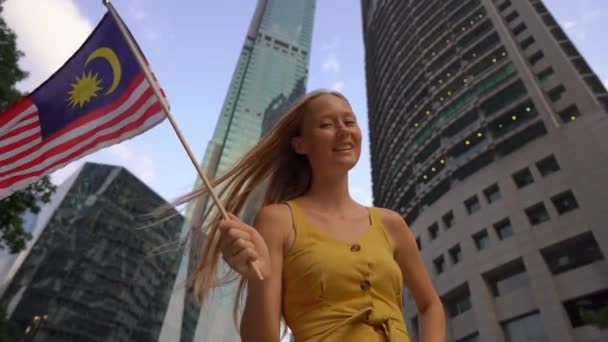 Fotografía en cámara lenta de una joven que ondea la bandera de Malasia con rascacielos en un segundo plano. Viajar a Malasia concepto — Vídeos de Stock