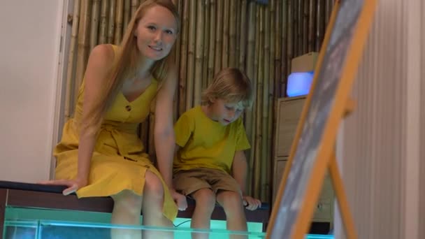 一个年轻女子和她的小儿子去参观鱼温泉。美容程序鱼剥皮 — 图库视频影像