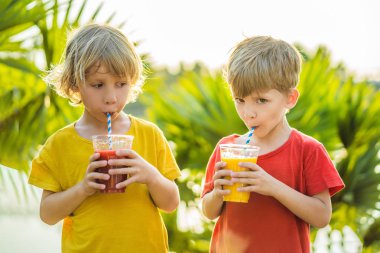 İki çocuk palmiye ağaçlarının arka planında sağlıklı meyve suyu içiyor. Mango ve karpuz püresi. Çocuklar için sağlıklı beslenme ve vitaminler