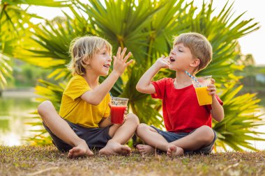 İki çocuk palmiye ağaçlarının arka planında sağlıklı meyve suyu içiyor. Mango ve karpuz püresi. Çocuklar için sağlıklı beslenme ve vitaminler