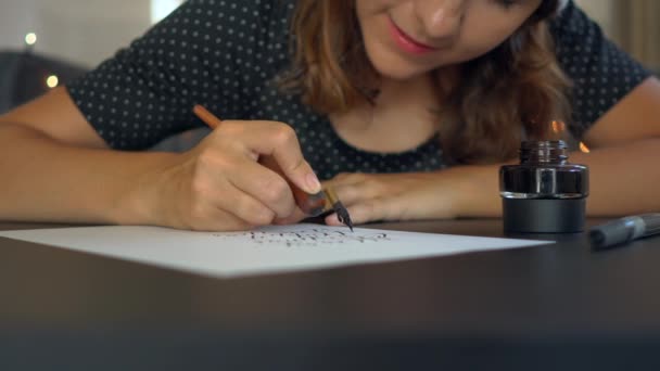 Close-up shot van een jonge vrouw kalligrafie schrijven op een papier met behulp van belettering techniek — Stockvideo