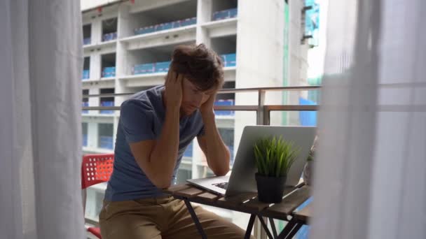 Scatto al rallentatore di un giovane seduto su un balcone con un quaderno e affetto da un forte rumore prodotto da un cantiere nelle vicinanze. Concetto di inquinamento acustico nelle grandi città — Video Stock