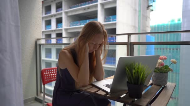 慢动作拍摄一名年轻女子坐在阳台上,带着笔记本,受到附近建筑工地的巨响影响。大城市噪声污染的概念 — 图库视频影像