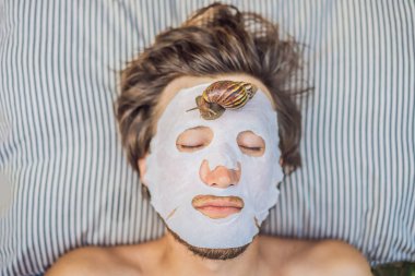 Genç adam salyangoz sümüğünden yüz maskesi yapıyor. Maskenin üzerinde sürünen bir salyangoz. Erkekler için spa, herkes için spa