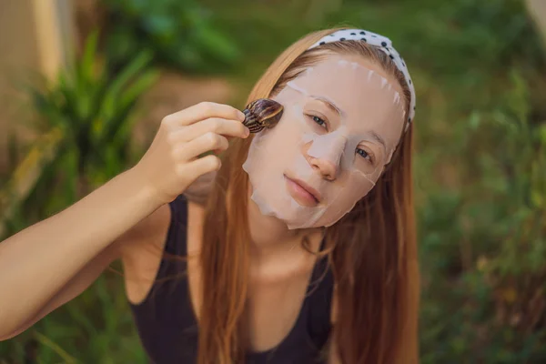 Μια νεαρή γυναίκα φτιάχνει μάσκα προσώπου με βλέννα σαλιγκαριού. Σαλιγκάρι σέρνεται σε μια μάσκα προσώπου — Φωτογραφία Αρχείου