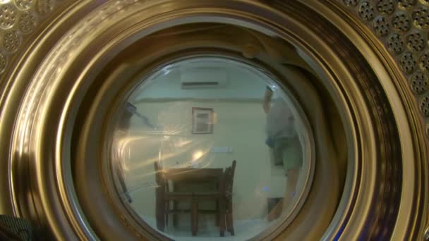 Вид з пральної машини, як молодий чоловік вкладає в неї брудний одяг — стокове відео