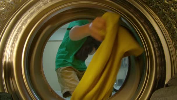 Uitzicht vanaf de wasmachine als een kleine jongen zet vuile kleren in het — Stockvideo