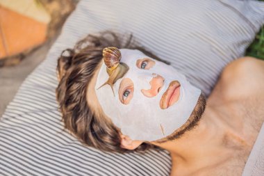 Genç adam salyangoz sümüğünden yüz maskesi yapıyor. Maskenin üzerinde sürünen bir salyangoz. Erkekler için spa, herkes için spa
