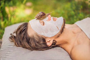 Genç adam salyangoz sümüğünden yüz maskesi yapıyor. Maskenin üzerinde sürünen bir salyangoz. Erkekler için spa, herkes için spa