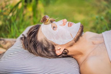 Genç adam salyangoz sümüğünden yüz maskesi yapıyor. Maskenin üzerinde sürünen bir salyangoz. Erkekler için spa, herkes için spa