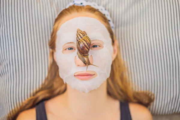 Young woman makes a face mask with snail mucus. Snail crawling on a face mask