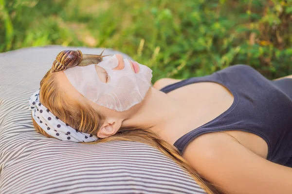 Genç kadın salyangoz sümüğüyle yüz maskesi yapıyor. Maskede sürünen bir salyangoz. — Stok fotoğraf
