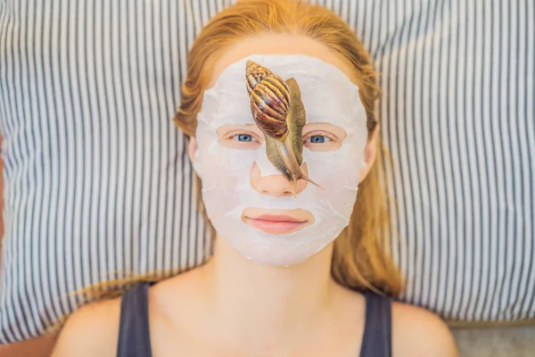 Young woman makes a face mask with snail mucus. Snail crawling on a face mask