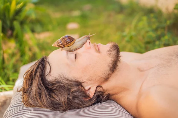 Young man makes a face mask with snail mucus. Snail crawling on a face mask. SPA for man, SPA for all — Stock Photo, Image