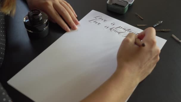 Close-up shot van een jonge vrouw kalligrafie schrijven op een papier met behulp van belettering techniek. Ze schrijft een bruiloft gelofte liefde is geduldig liefde is vriendelijk — Stockvideo