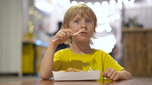 Närbild skott av en liten pojke som äter en välsmakande våffla i ett gatukafé. Gatukost koncept — Stockvideo