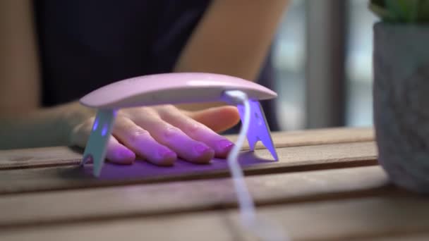 Zbliżenie strzał kobiety robi jej manicure za pomocą żelu Polski, który twardnieje w świetle ultrafioletowym — Wideo stockowe