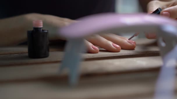 Primer plano de una mujer haciendo su manicura usando gel pulido que se endurece bajo luz ultravioleta — Vídeos de Stock