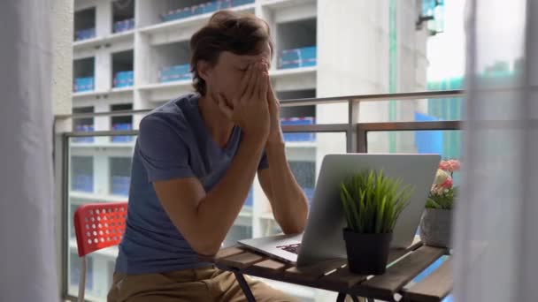 Jovem sentado em uma varanda com um caderno e sofrendo de um barulho alto produzido por um canteiro de obras nas proximidades. Conceito de poluição sonora nas grandes cidades — Vídeo de Stock