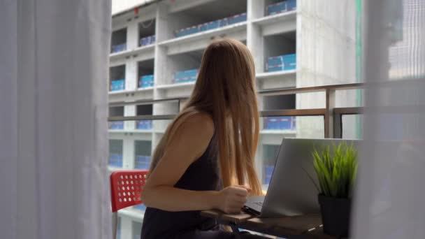 Ung kvinna sitter på en balkong med en anteckningsbok och lider av ett högt ljud som produceras av en byggarbetsplats i närheten. Begreppet bullerförorening i storstäderna — Stockvideo