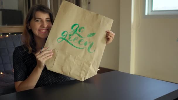 Крупный план молодой женщины-каллиграфа, пишущей на бумажном пакете с использованием техники письма. Она пишет "Го зеленый". Сокращение использования пластика — стоковое видео
