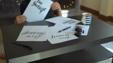 Genç bir kadın kaligrafi yazı yazma tekniği kullanarak bir kağıt üzerinde çekim yakın. O kelimeleri ile çarşafları bakıyor kendini sev ve gülüyor
