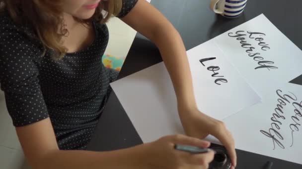 Nahaufnahme einer jungen Frau, die in Schrifttechnik auf ein Papier schreibt. Sie schreibt die Liebe selbst — Stockvideo