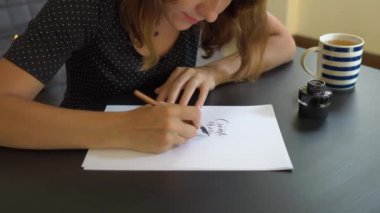 Genç bir kadın kaligrafi yazı yazma tekniği kullanarak bir kağıt üzerinde çekim yakın. O writtes oluşturmak daha