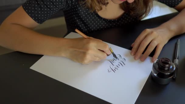 Close-up shot van jonge vrouw in een kerstmuts kalligrafie schrijven op een papier met behulp van belettering techniek. ze schrijft Merry Christmas — Stockvideo
