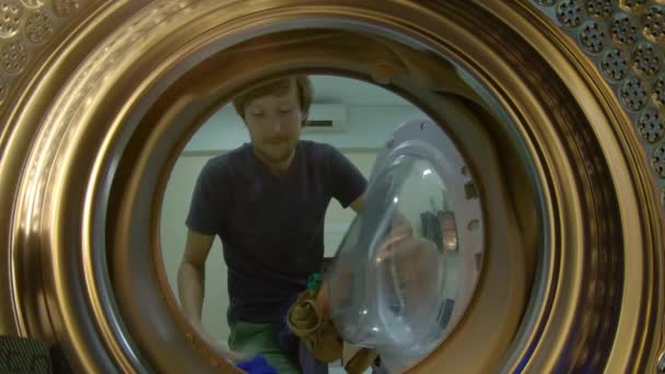 Blick aus der Waschmaschine, als ein junger Mann schmutzige Wäsche hineinlegt — Stockvideo