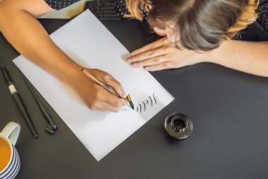 Hattat genç kadın beyaz kağıda ifade yazıyor. Süs dekorasyonlu mektuplar. Kaligrafi, grafik tasarım, yazı, el yazısı, Yaratılış konsepti