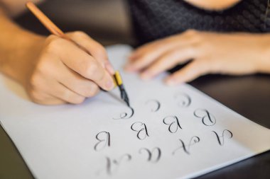 Hattat genç kadın beyaz kağıda ifade yazıyor. Süs dekorasyonlu mektuplar. Kaligrafi, grafik tasarım, yazı, el yazısı, Yaratılış konsepti