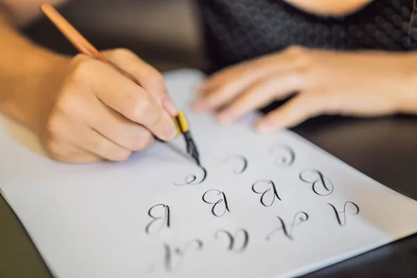 Kalligrafka mladá žena píše frázi na bílém papíře. Vepisující ozdobná písmena. Kaligrafie, grafický design, písmo, rukopis, koncepce tvorby — Stock fotografie