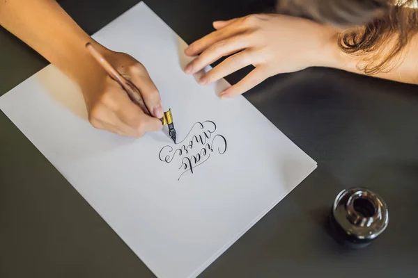 Crea más. Calígrafa Joven escribe frase en papel blanco. Inscribiendo letras ornamentales decoradas. Caligrafía, diseño gráfico, letras, escritura a mano, concepto de creación —  Fotos de Stock