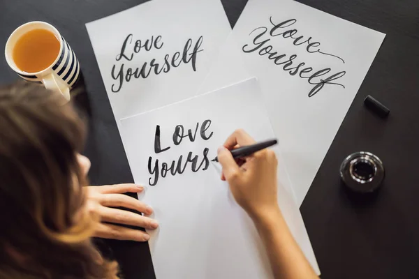 Love yourself. Calligrapher Young Woman writes phrase on white paper. Inscribing ornamental decorated letters. Calligraphy, graphic design, lettering, handwriting, creation concept