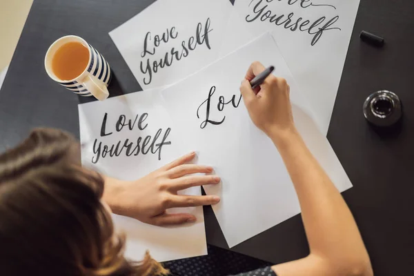 Love yourself. Calligrapher Young Woman writes phrase on white paper. Inscribing ornamental decorated letters. Calligraphy, graphic design, lettering, handwriting, creation concept